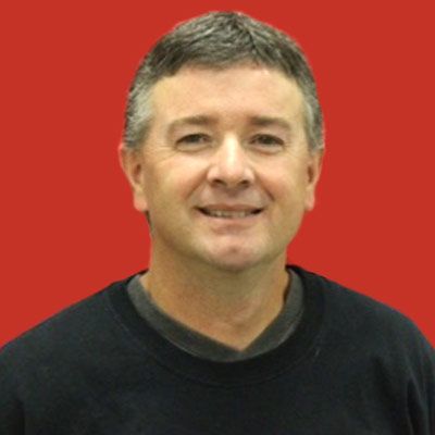 Smiling man with short hair wearing a dark sweatshirt, posed in front of a solid red background.